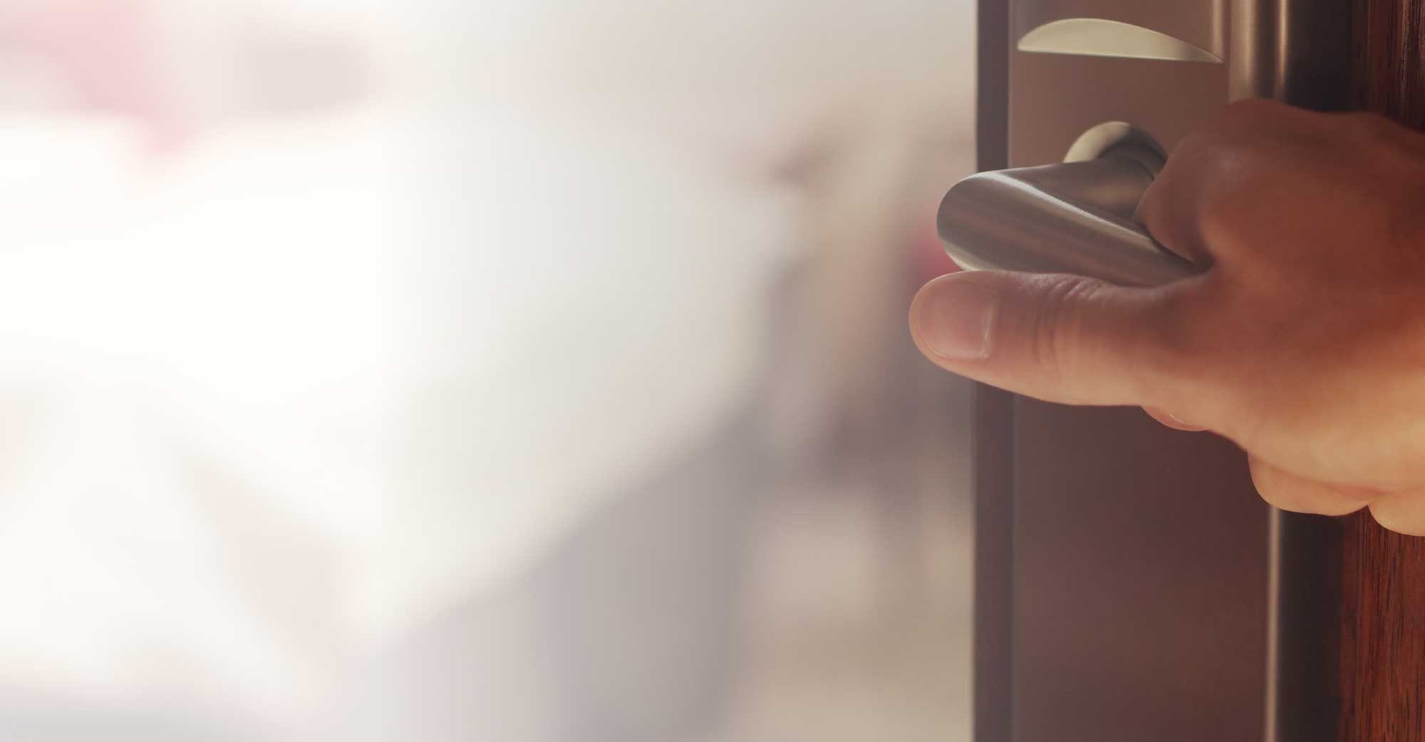 Männliche Hand an der Türklinke öffnet die Tür zu einem Hotelzimmer mit Doppelbett