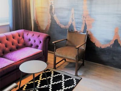 Sitzecke mit einem pinken Sofa und einem altmodischen Stuhl vor einer Wand  mit goldener und grauer Farbgestaltung