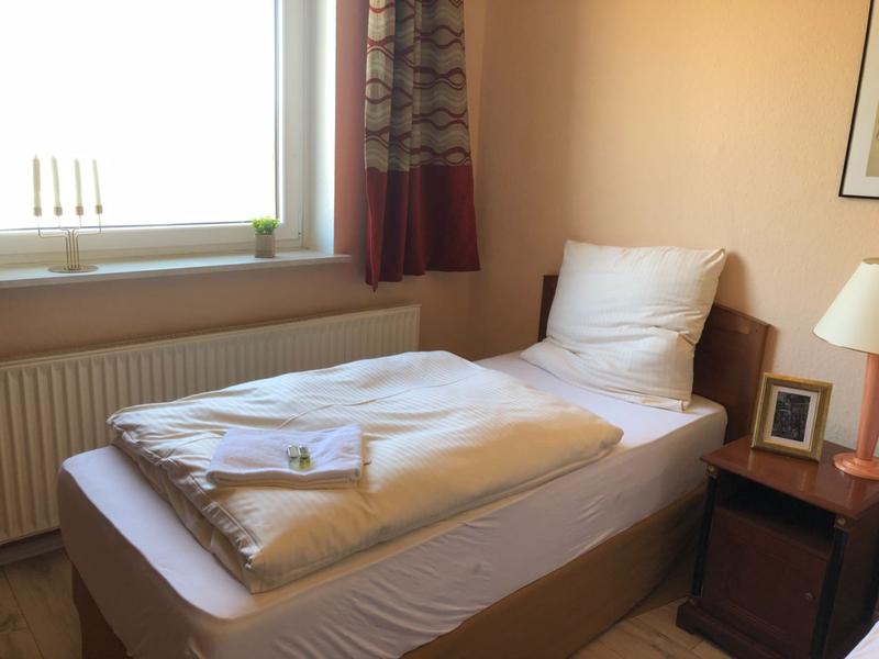 Einzelbett mit Nachttisch direkt neben einem Fenster