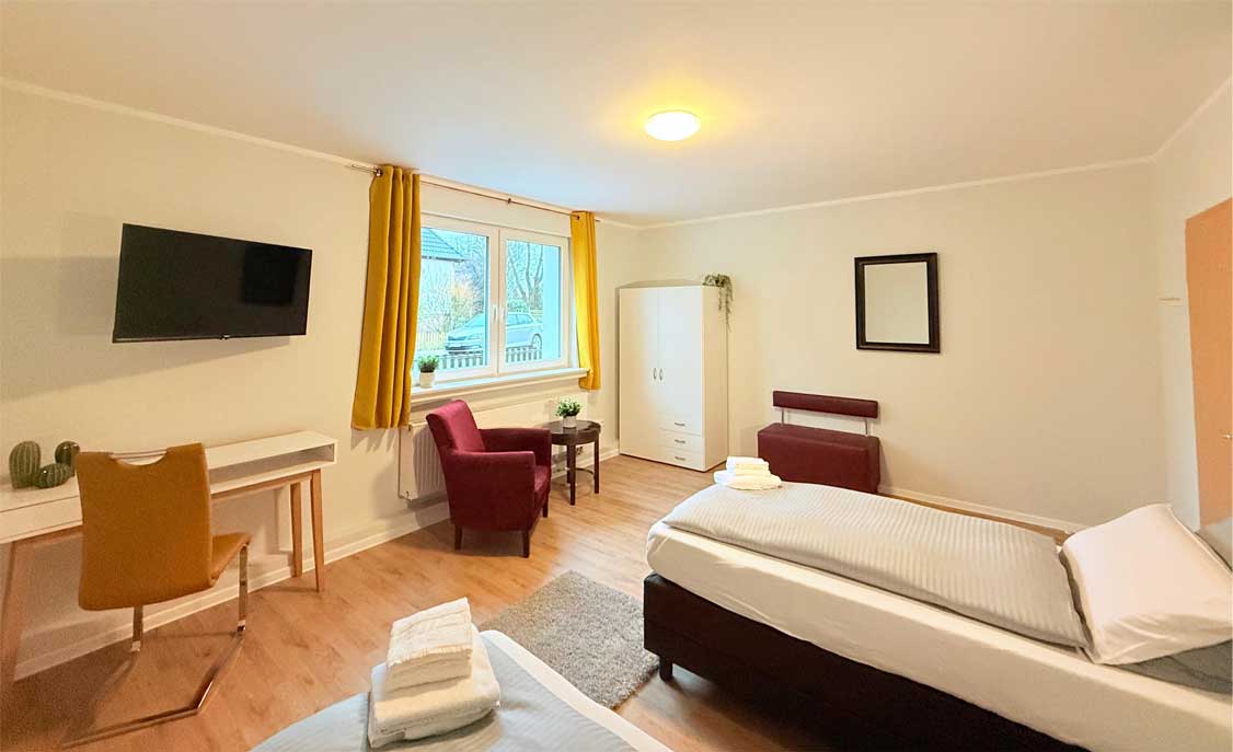 Blick vom Bett eines Zweibettzimmers mit Sitzbereich und Schreibtisch