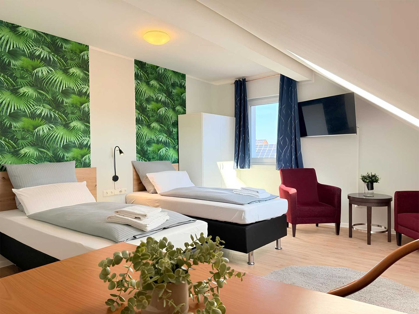 Modernes Zweibettzimmer mit Wandgestaltung hinter den Betten und Sitzbereich